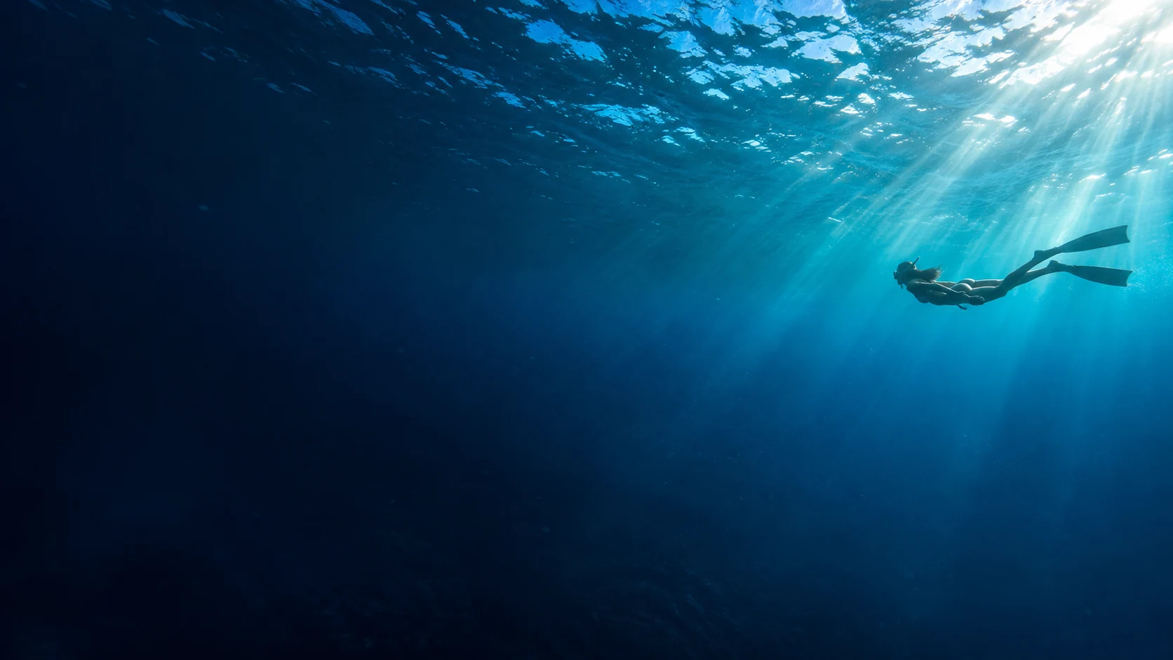 A freediver gliding through clear blue water beneath sunlit ocean ripples